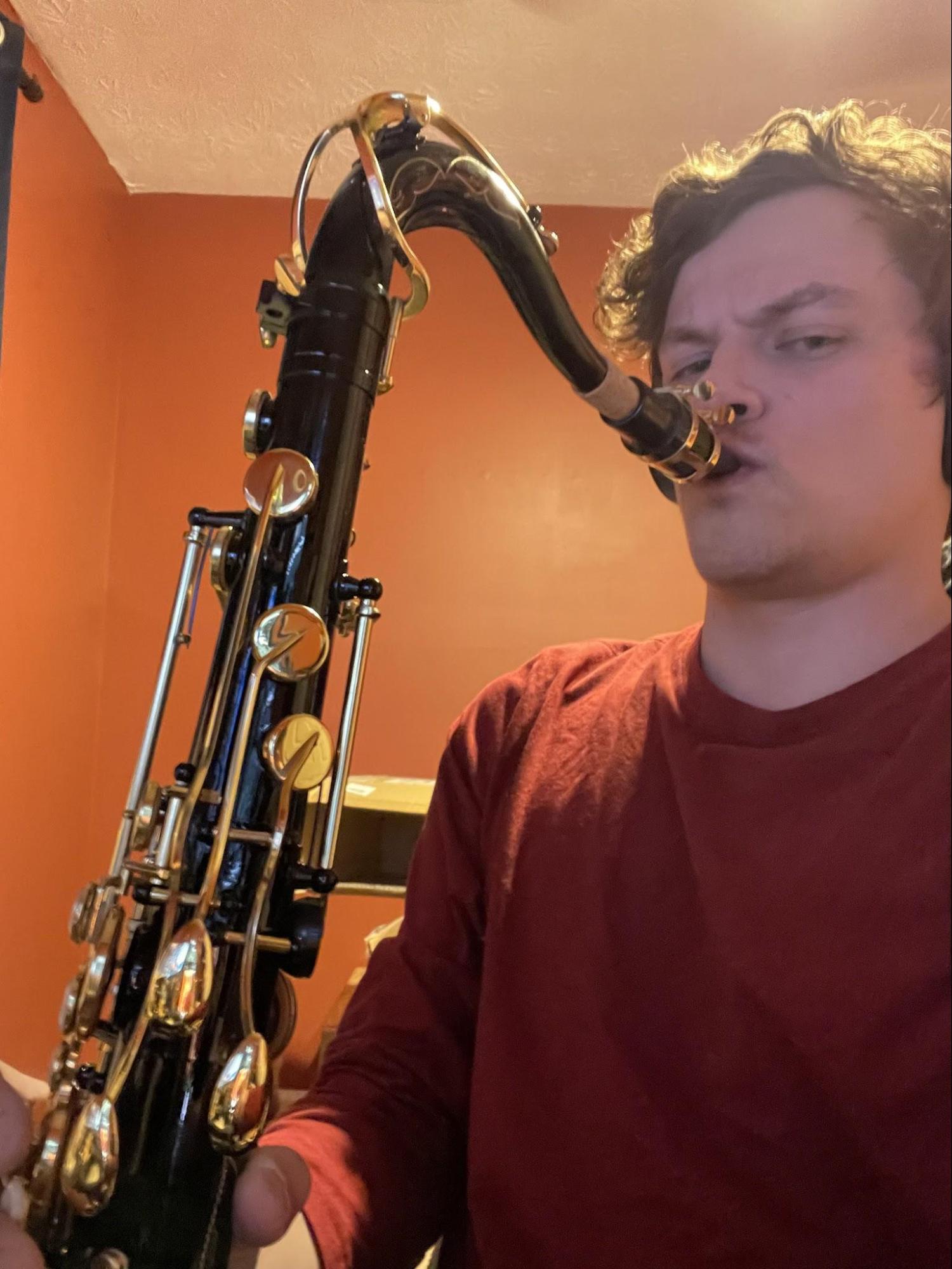 ryan with his mouth to a saxophone, looking grumpily confused at the camera